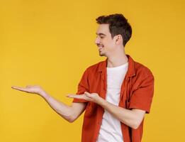 Portrait of happy smiling young man presenting and showing your text or product isolated on yellow background photo