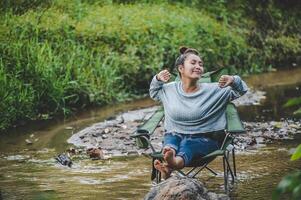 Young woman sitting on camping chair in stream for relax photo