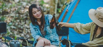 Young women sitting and drink beverage  front of camping tent photo