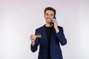 Portrait of happy handsome businessman talking by mobile phone and holding credit card isolated over white background photo