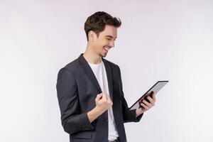 Portrait of attractive cheerful businessman doing winner gesture clenching fist and using device app searching web isolated over white color background photo