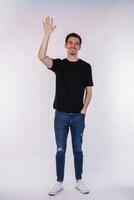 Portrait of friendly cheerful man in black t-shirt and jeans saying hi, welcome person as waving hand photo