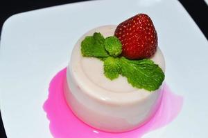 A close up image of strawberry pudding with mint and strawberry on top in a white plate photo