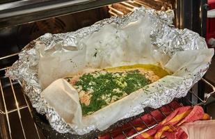 salmón con ajo y hierbas es horneado en el horno en hoja con frustrar horneando papel foto