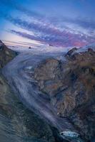 un enorme montaña glaciar durante puesta de sol con púrpura nubes foto