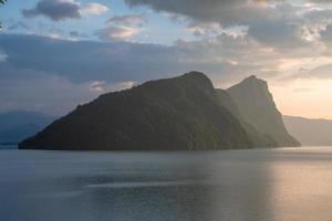 A green mountain standing by a lake during the sunset photo