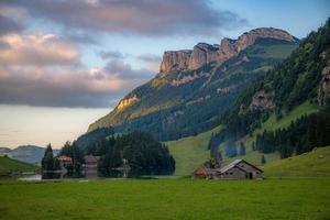 Farm houses stand on the edge of a lake surrounded by mountains at sunset photo