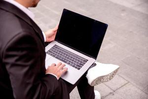 joven chico en un traje trabajos en un computadora en el parque, ordenador portátil cerca arriba foto