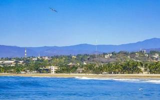 Sun beach cliffs rocks waves palms mountains Puerto Escondido Mexico. photo