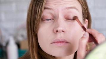 diario constituir. natural belleza. joven mujer sin maquillaje mirando a el espejo cepillado su Cejas con ceja lápiz, amarillo mimosa flores un el antecedentes video