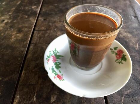 A glass of coffee on a wooden table with a flower pattern on the rim. photo