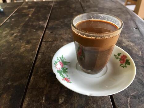 A glass of coffee on a wooden table with a flower pattern on the rim. photo