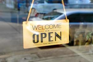 welcome we are open please come in sign on the glass door of the coffee shop photo