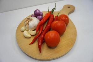 Garlic, Chili, red onion and tomatoes on a wooden coaster, High Angle shot. photo