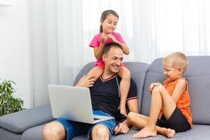Children with father looking at the screen of laptop computer, home education concept photo