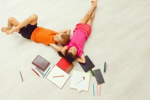 Happy children. Top view creative photo of little boy and girl on vintage brown wooden floor. Children lying near books and toys, and painting