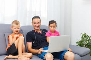 Father with two cute children sitting on sofa and using laptop together photo