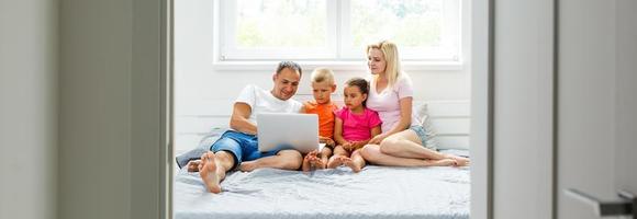 Portrait of Asian family looking at a tablet computer while lying on the bed, little asian girl using laptop with her parents. Weekend holiday leisure time education concept photo