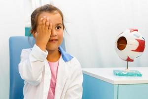 Close up portrait of girl reviewing eyesight closing eye with hand.Out of focus test chart in background. photo