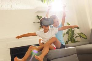 Adorable little children using virtual reality headsets while sitting on sofa at home photo