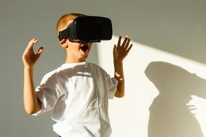 asombrado pequeño chico mirando en un vr gafas de protección y gesticulando con su manos aislado en blanco antecedentes foto