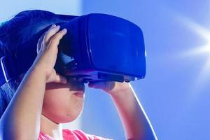 Young girl experiencing VR headset game on colorful background. Child using a gaming gadget for virtual reality. Futuristic goggles at young age. Virtual technology photo