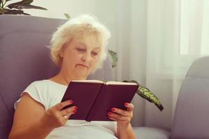 Happy senior woman reading book on her sofa at home photo