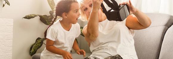 abuela y nieta. contento antiguo mujer jugando virtual realidad con pequeño niña a hogar. realidad virtual, aumentado realidad vídeo y tecnología. foto