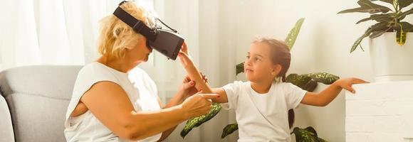 familia relación Entre abuela y nieta. contento antiguo mujer jugando virtual realidad con pequeño niña a hogar. realidad virtual, aumentado realidad vídeo y tecnología. foto