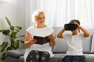 Family relationship between grandmother and granddaughter. Happy old woman playing virtual reality with little girl at home. VR, Augmented Reality video and technology. photo