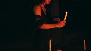 a woman in black is lighting a candle that goes out in the dark