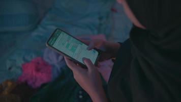 un' musulmano donna prende un' inteligente Telefono su il letto e risposte per messaggi a partire dal sua amico video