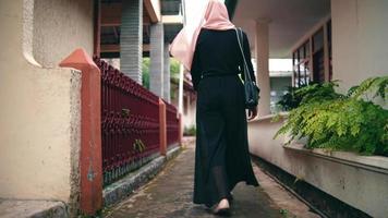 uma muçulmano mulher com uma Rosa lenço de cabeça e uma Preto camisa é caminhando dentro a beco video