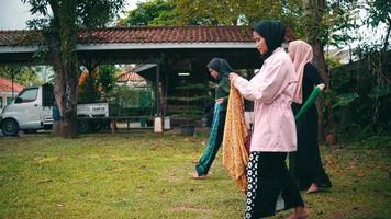 un grupo de musulmán mujer corbatas un estampado paño alrededor su cintura antes de haciendo danza práctica en el jardín video