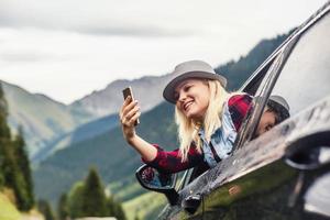 Smiling young woman taking selfie picture with smart phone camera outdoors in car photo