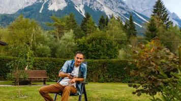 Young man relaxing on sun lounger near river and mountains. photo