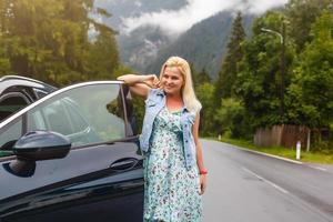 Woman with car near countryside road through mountain Alps photo