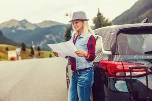 Toward adventure. Beautiful young woman checks the route on a map on the sunset background. photo