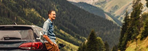 Handsome young man standing outdoors near his car and . Young man on road trip photo