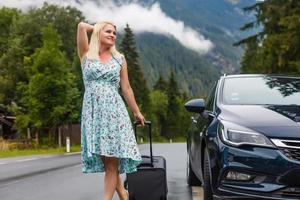 woman in the summer goes on vacation, on vacation with an suitcase on the background of nature and mountains. The concept of travel, weekend in a beautiful place in the mountains photo