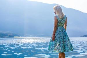 Young woman standing with backpack on cliff's edge and looking to a sky photo