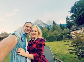 tourism, travel, people, leisure and technology concept - happy international teenage couple taking selfie over alps mountains in austria background photo