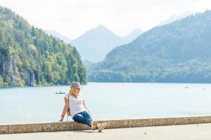 Beautiful tourist lady wearing hat and backpack enjoying stunning view on Bavarian mountains near Neuschwanstein castle in Germany. Traveling concept. Nature view photo