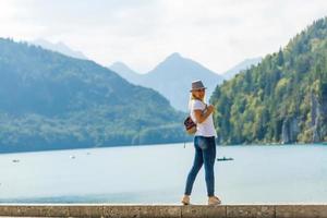 hermosa turista dama vistiendo sombrero y mochila disfrutando maravilloso ver en bávaro montañas cerca Neuschwanstein castillo en Alemania. de viaje concepto. naturaleza ver foto