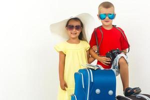 Children travel - boy with a camera, girl in sunglasses and white hat stand near a suitcase photo