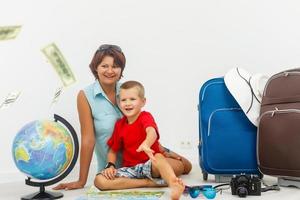 Family travel - young woman and boy sitting, lookin at a globe, while dollar banknotes fall photo