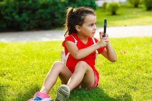 Cute little girl looking at grass through magnifying glass photo