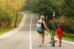 Happy mother and baby girl having fun in park with bicycle photo