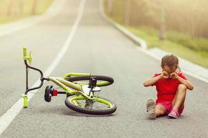 un pequeño niña montando un bicicleta. el bicicleta accidente. sentar llorando en el calle foto