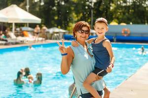 Close-up portrait of beautiful mother with her son standing swimming pool and laughing during vacation on warm summer day photo